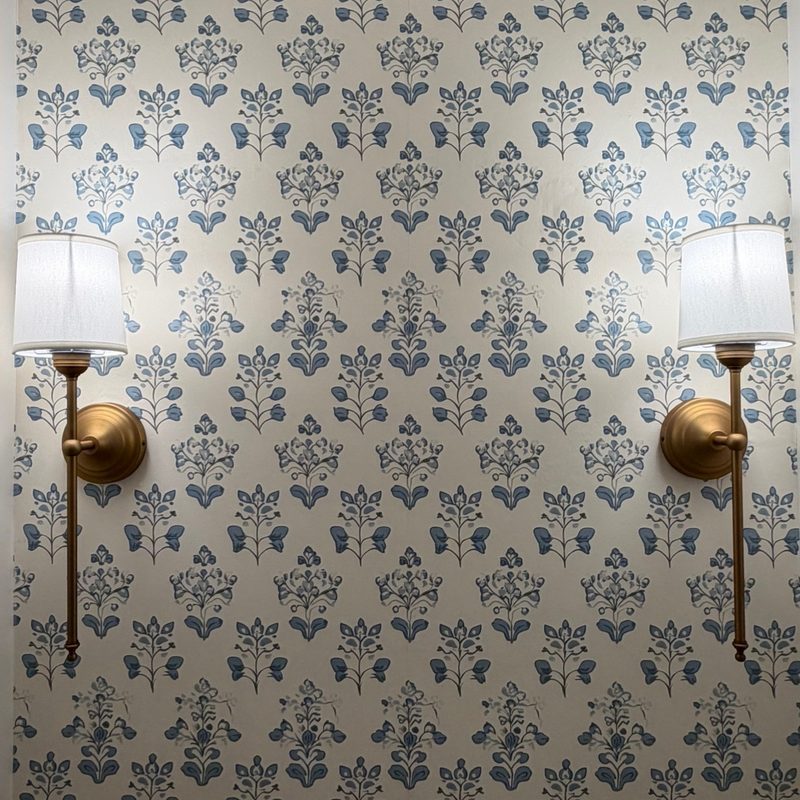 Two brass wall sconces with white shades, mounted level on a papered wall.