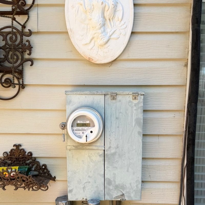 An old galvanised meter can and meter, weathered, on cream lap siding.