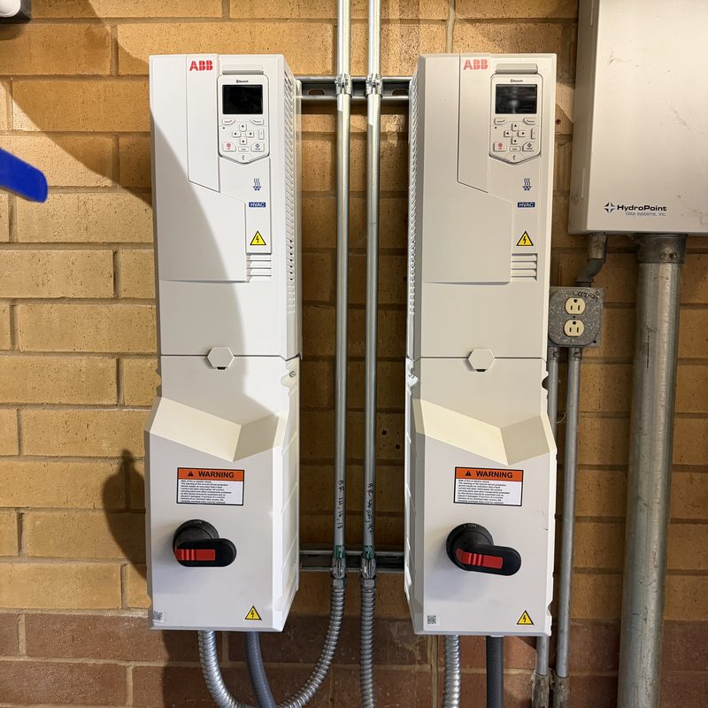 Two white ABB variable frequency drives with disconnect handles, mounted on a brick wall.